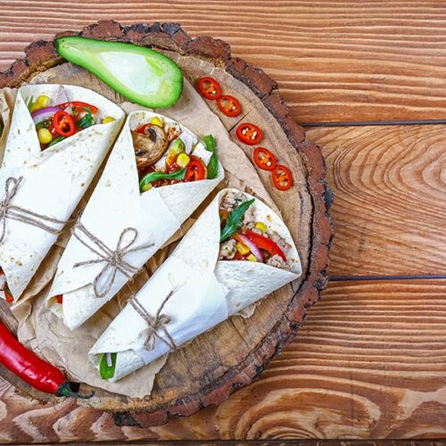 Three vegetable wraps with avocado and chili on a wooden board.