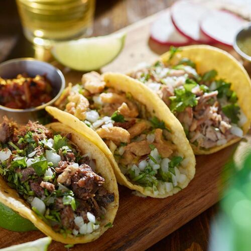 Three delicious tacos filled with meat, onions, and cilantro on a wooden board.