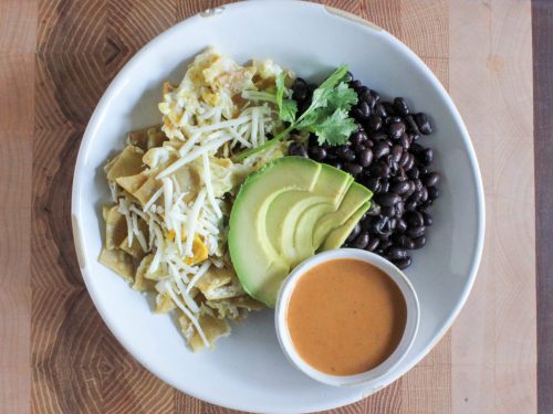 A bowl with shredded chicken, black beans, avocado slices, and a dipping sauce.