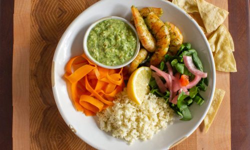 A plate with shrimp, guacamole, rice, salad, and carrot ribbons.